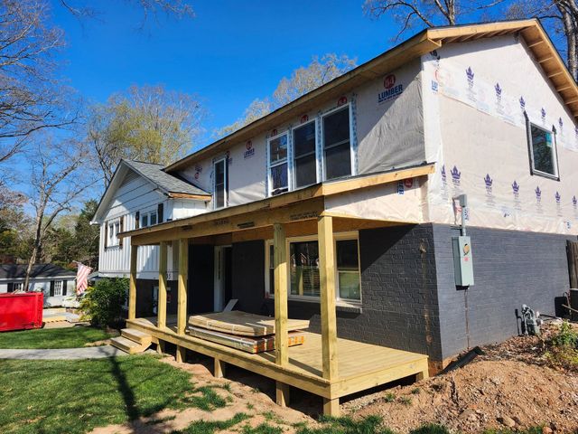 House with a partially built wooden porch and deck in a yard, under construction on a sunny day