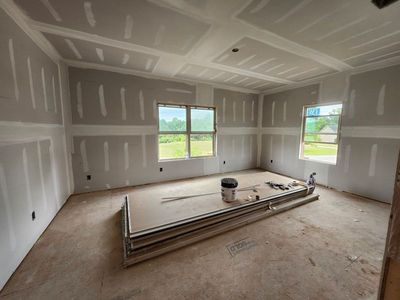 Unfinished drywall room with bare floors, a window, and stacked building materials in the center