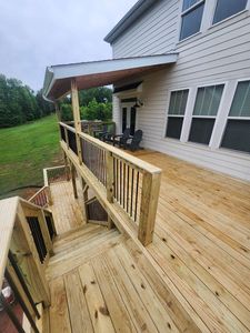 Wooden deck with stairs and railing beside a white house, overlooking a grassy yard.