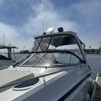 A white motorboat with a clear windshield is docked on a sunny day. The background features blue sky and water. A white motorboat with a clear windshield is docked on a sunny day. The background features blue sky and water.