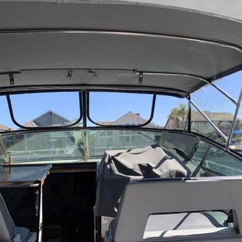 Interior view of a boat cockpit with windows overlooking houses and a blue sky. A seat is covered by a gray tarp. Interior view of a boat cockpit with windows overlooking houses and a blue sky. A seat is covered by a gray tarp.