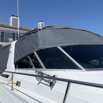 A close-up of a white boat with a dark gray canvas covering the windshield and cabin. The boat is in a sunny outdoor setting. A close-up of a white boat with a dark gray canvas covering the windshield and cabin. The boat is in a sunny outdoor setting.