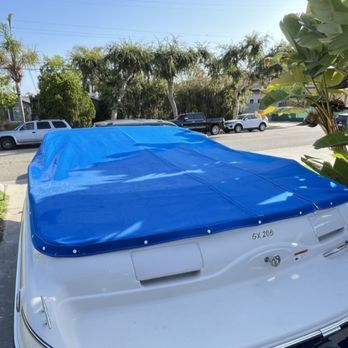 A white boat with a blue cover is parked in a driveway. Trees and houses are in the background. A white boat with a blue cover is parked in a driveway. Trees and houses are in the background.