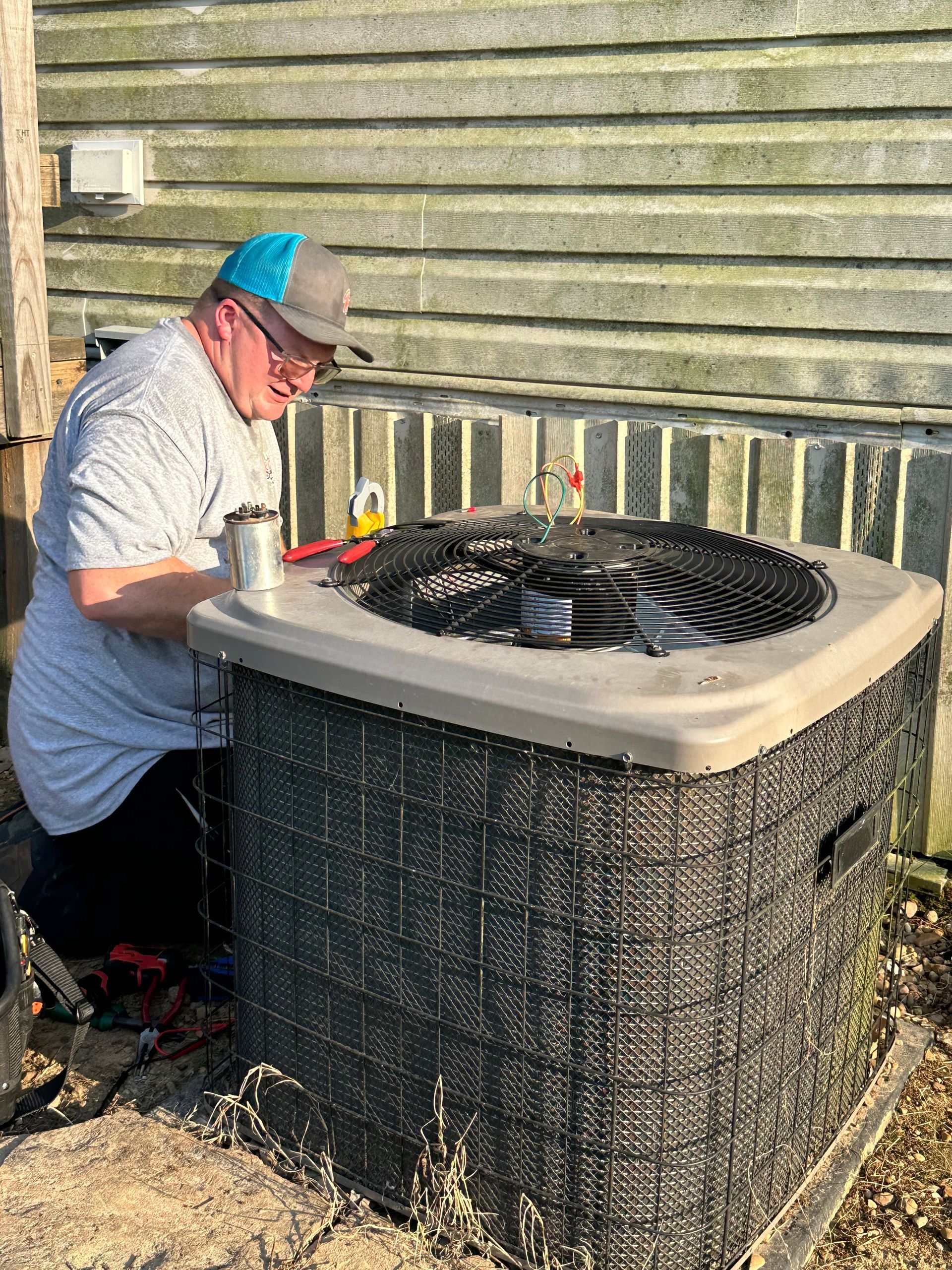 Technician cleaning an outdoor HVAC unit beside a building wall