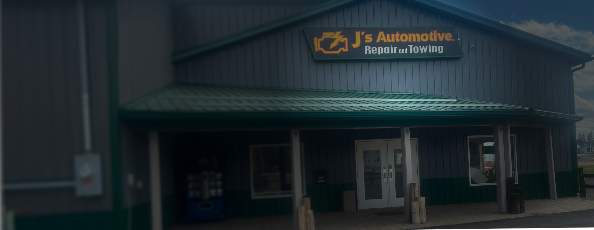 A gray auto repair shop building with two garage bays, parked cars, and a sign for