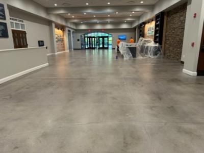 Large, empty room with polished concrete floor, two people in orange vests, and entrance to outdoor area.