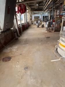 Concrete factory floor with pipes, equipment, and red fire hose.