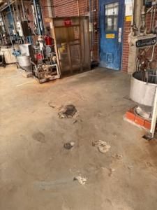 Industrial floor with stains and debris near equipment and a blue door.