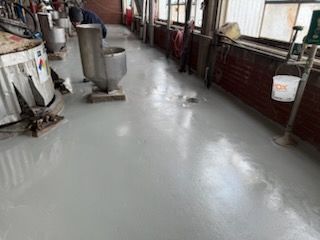 Gray industrial floor in a factory. Silver vats and a bucket are in the setting.