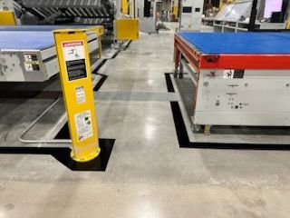 Yellow safety pole with black square, near industrial machinery, on a factory floor.
