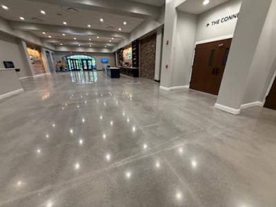 Polished concrete floor in a large building lobby.  A welcoming entrance with brown doors, dark counter and recessed lighting.