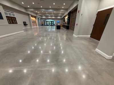 Spacious, polished concrete floor in a large lobby, leading to a glass entrance and front desk.