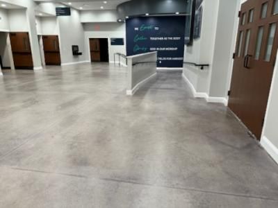 Spacious lobby with polished concrete floor, brown doors, and teal wall with text.