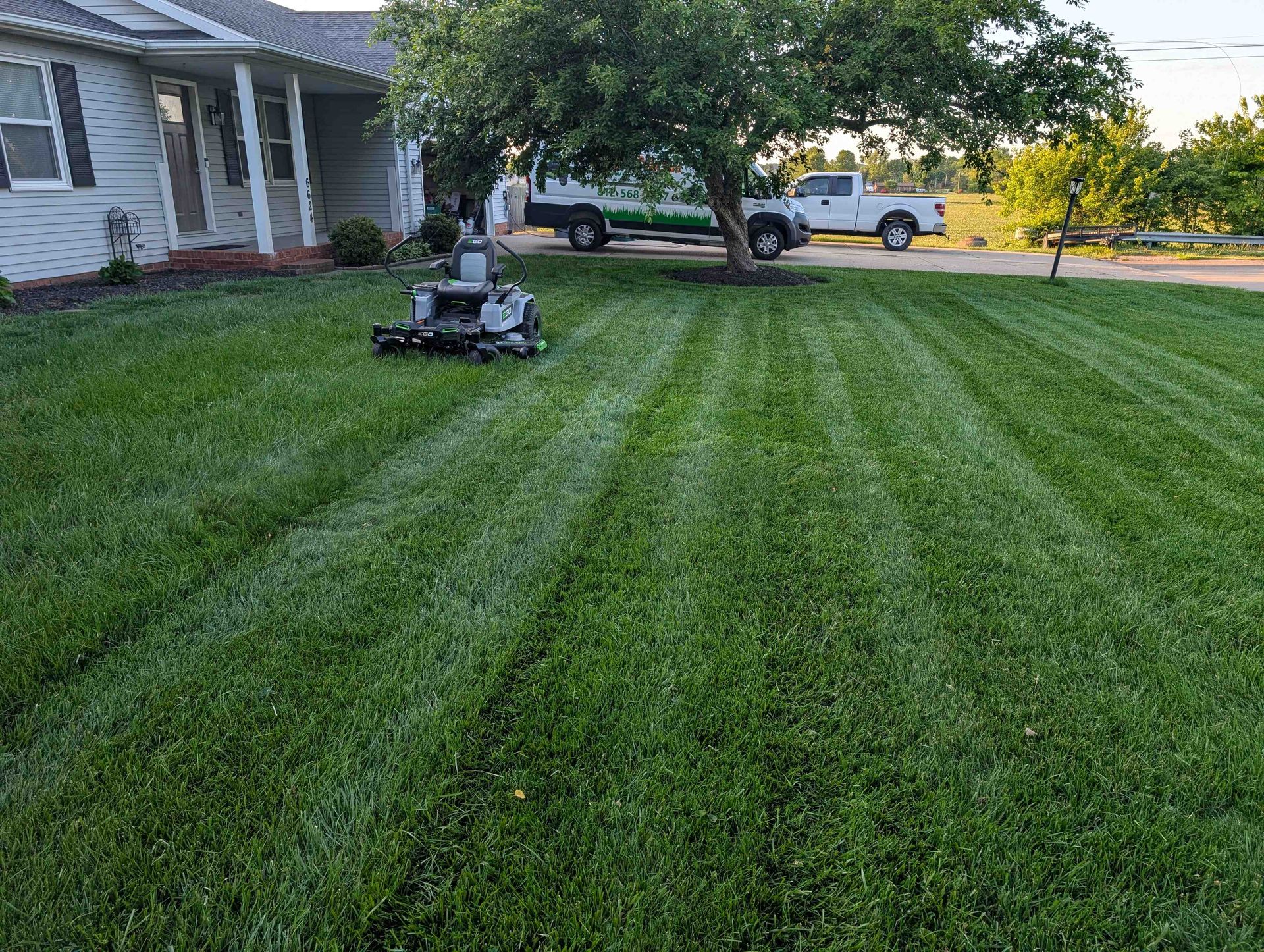 Lawn mower cutting striped green grass beside a house in a suburban yard