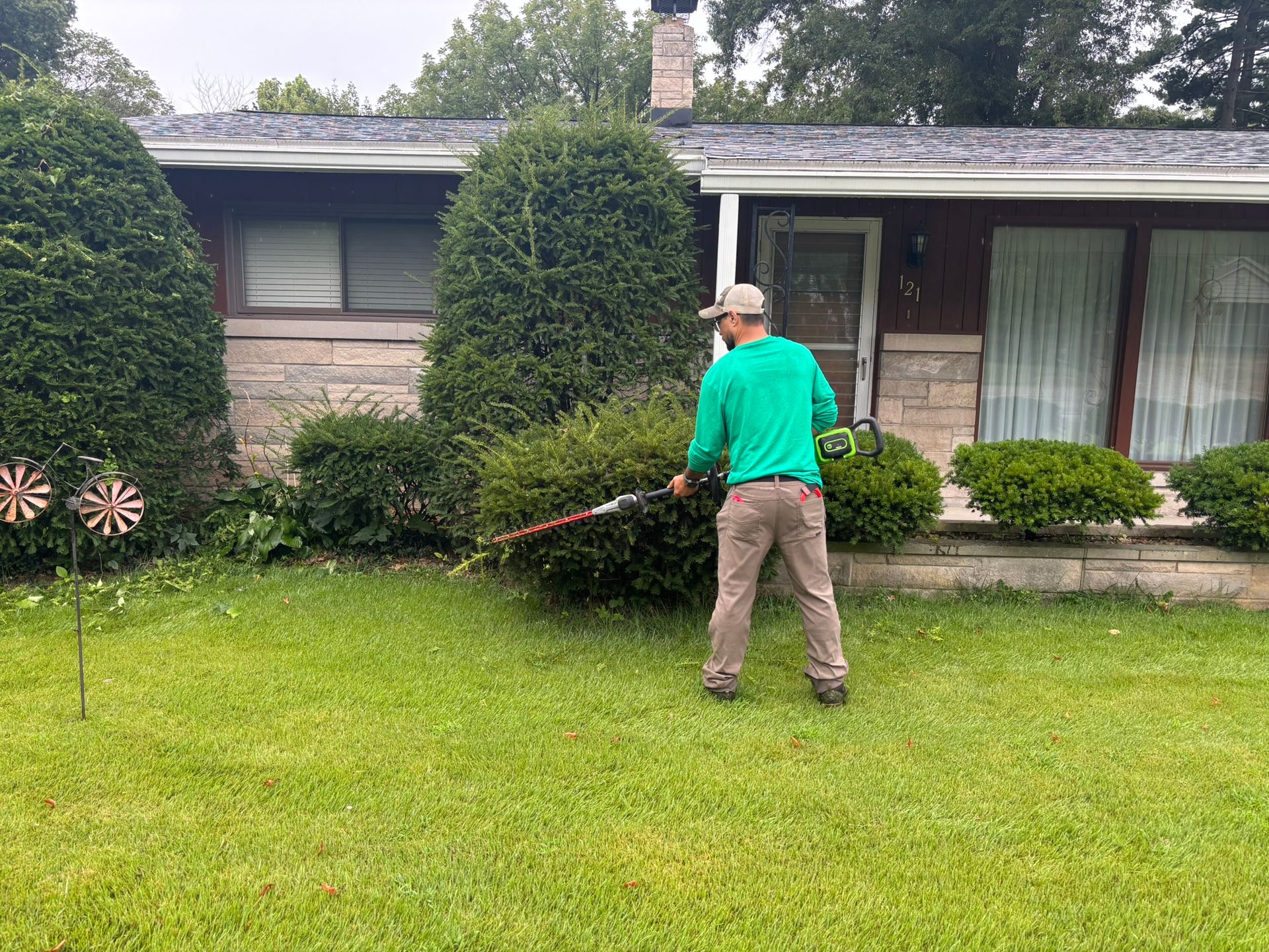 Person using a string trimmer on a front lawn in front of a house