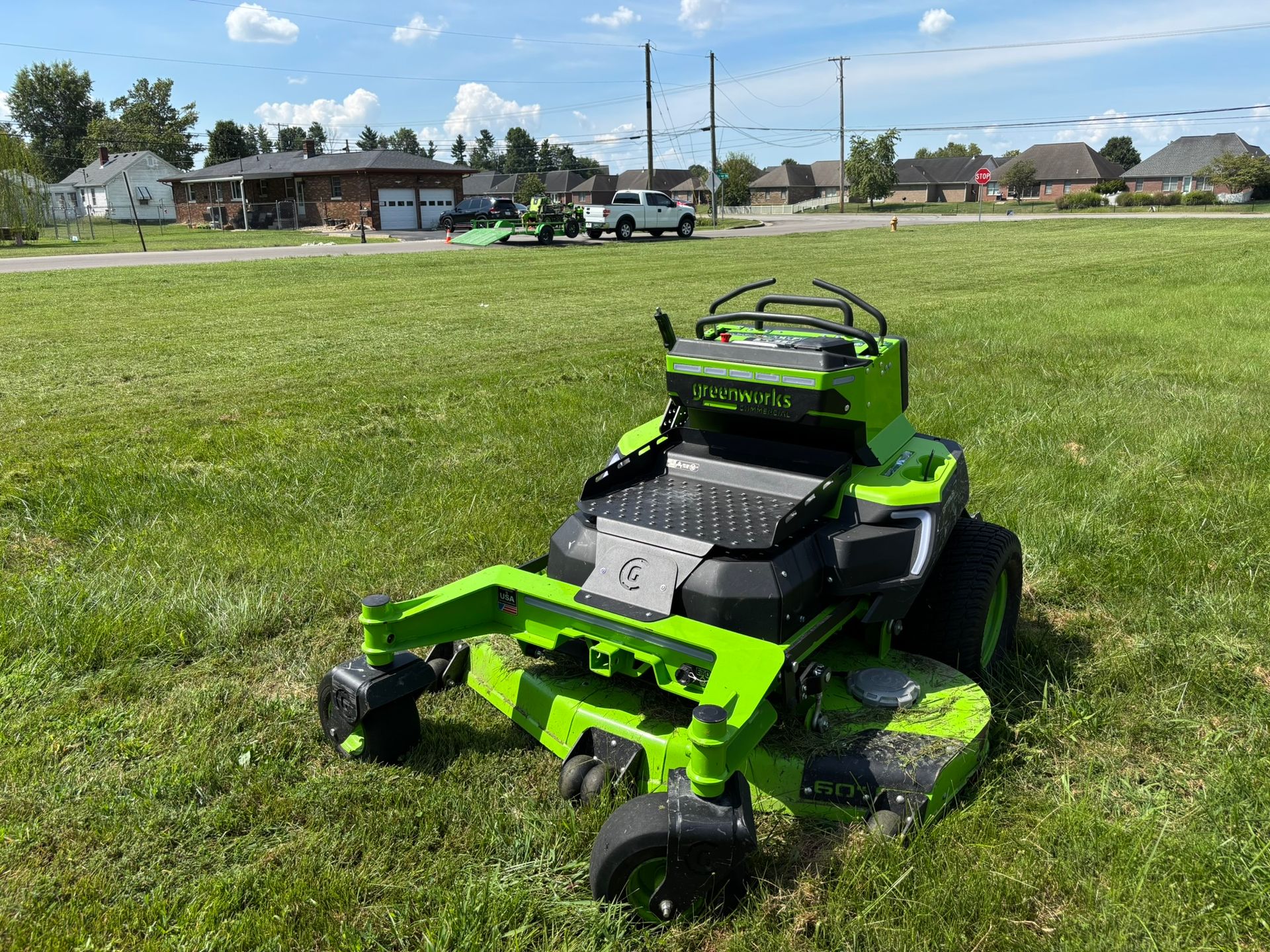 Bright green riding lawn mower on a grassy field under a blue sky