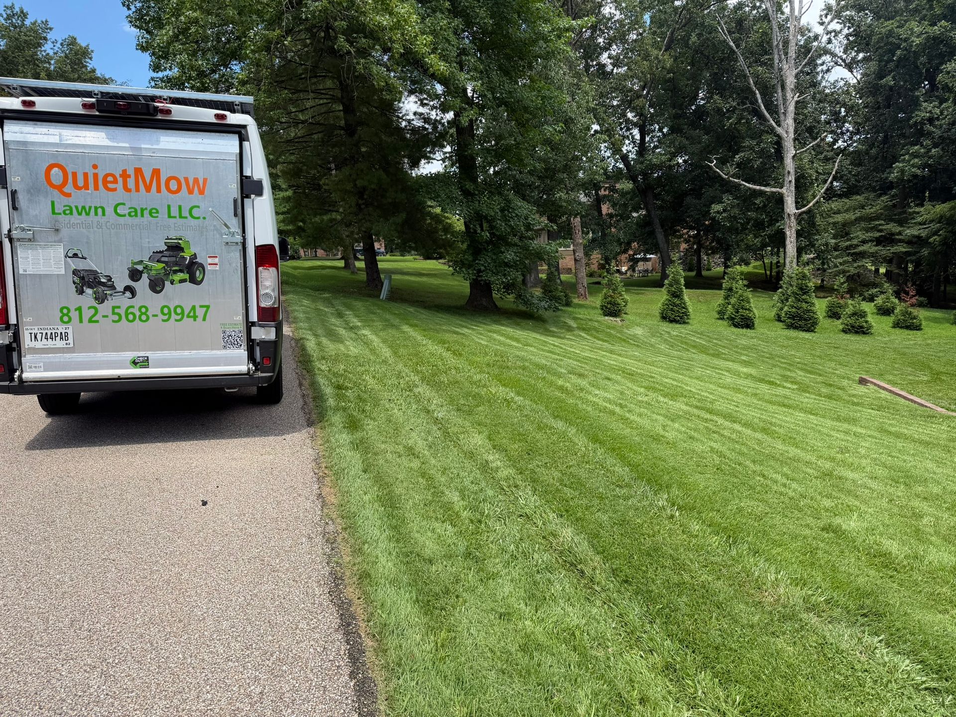 Lawn care van parked beside a freshly mowed grassy yard and tree-lined road.