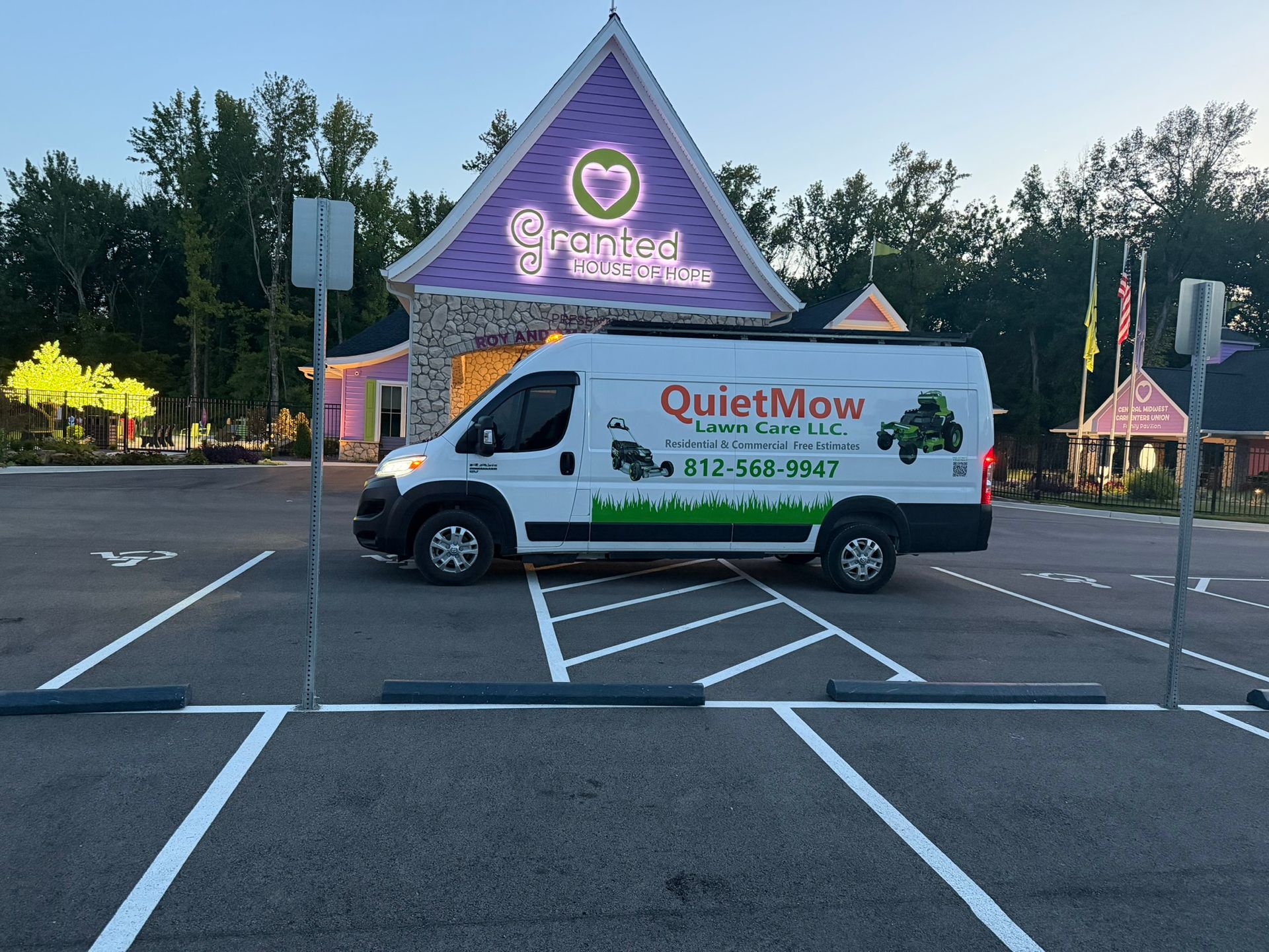 White QuietMow van parked in front of a purple storefront at dusk, with lights on and empty parking spaces.