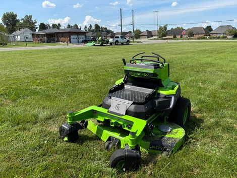 Bright green lawn mower on a grassy field near houses under a blue sky
