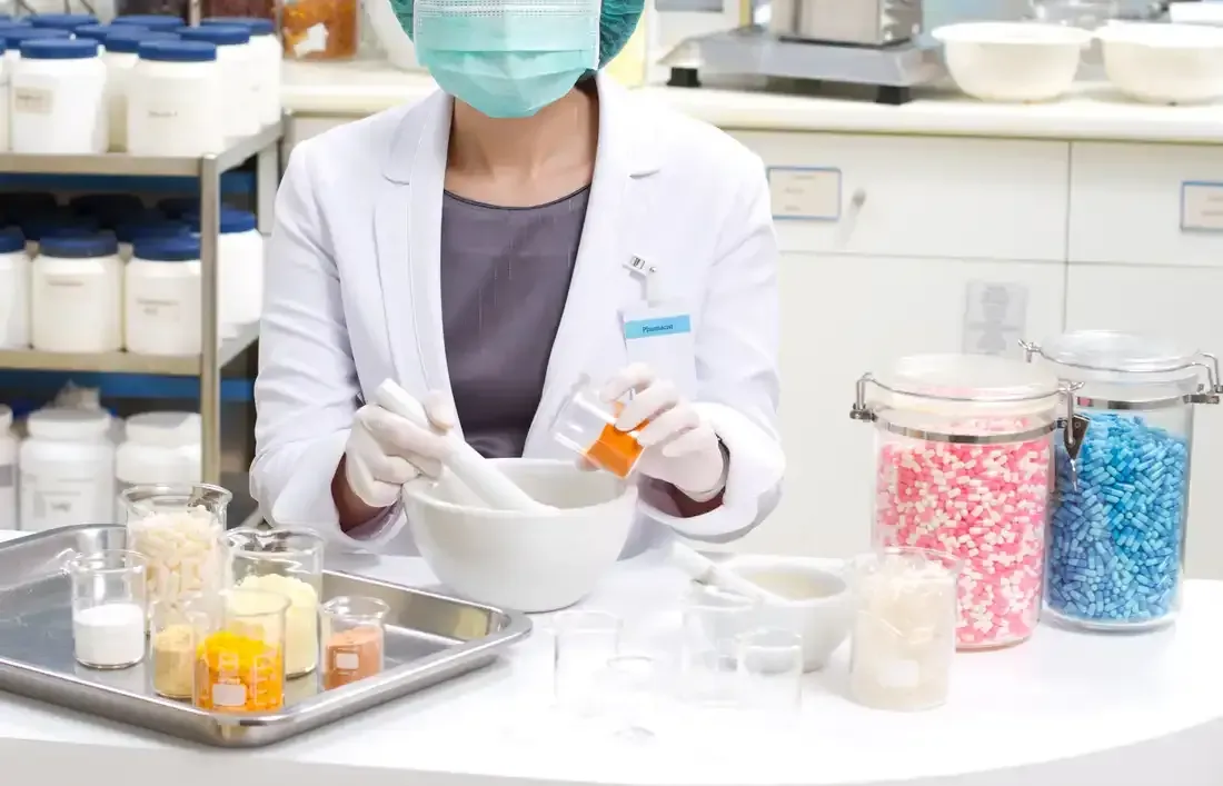 A female pharmacist wearing a mask and gloves is mixing ingredients in a mortar and pestle.