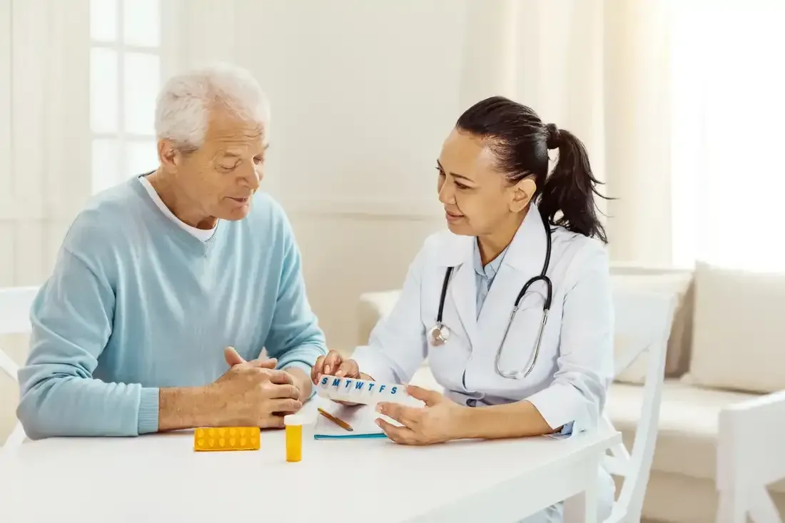 A doctor is talking to an elderly man while sitting at a table.