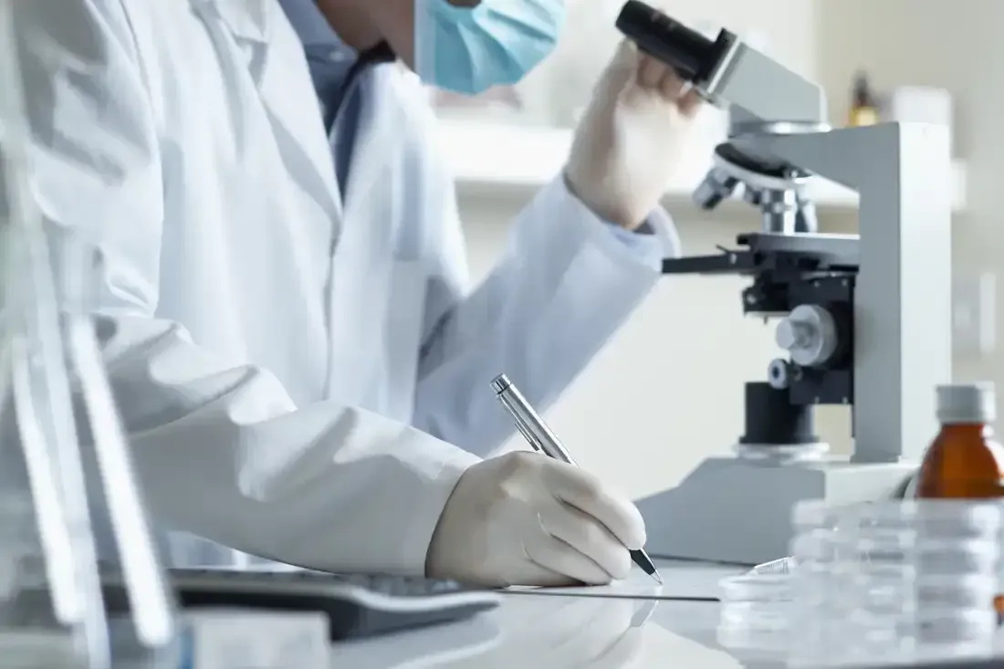 A scientist is looking through a microscope and writing on a piece of paper.