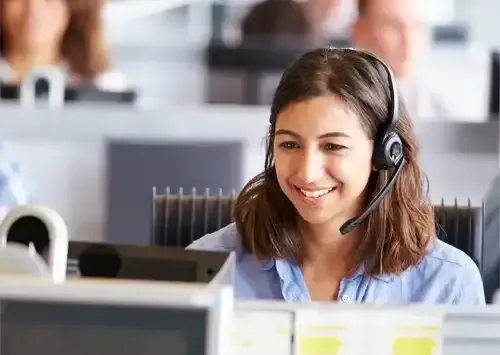 Femme portant un casque audio dans un bureau, souriante et regardant un écran d'ordinateur.