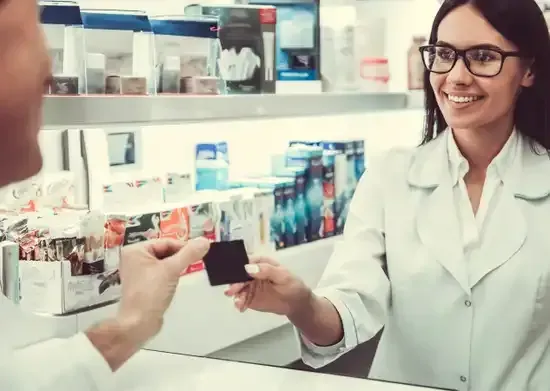 A woman is giving a credit card to a man in a pharmacy.