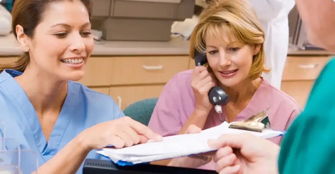 Two nurses are talking on the phone while another nurse looks at a clipboard.
