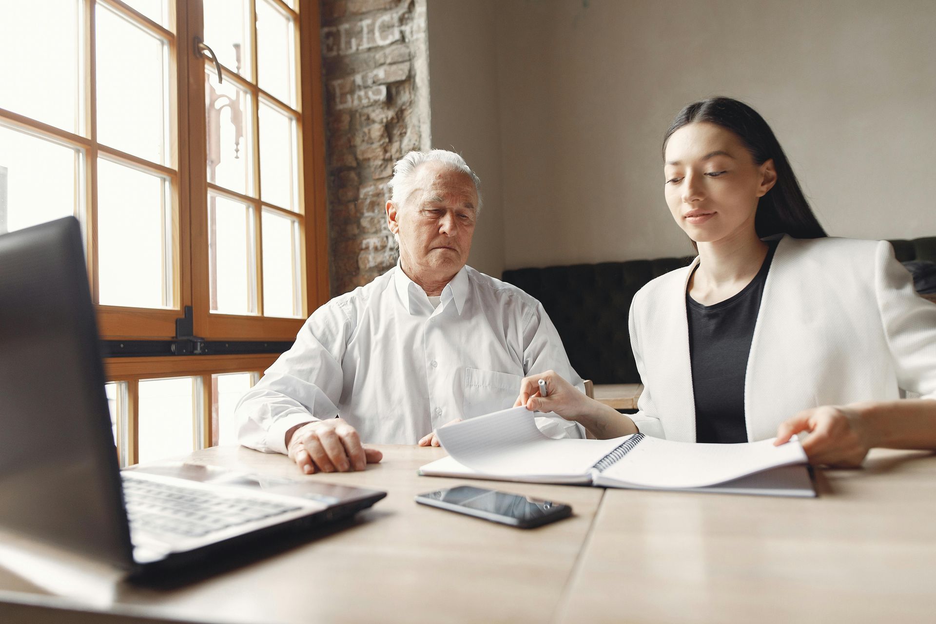 Two people reviewing documents at a desk with a laptop in a bright office