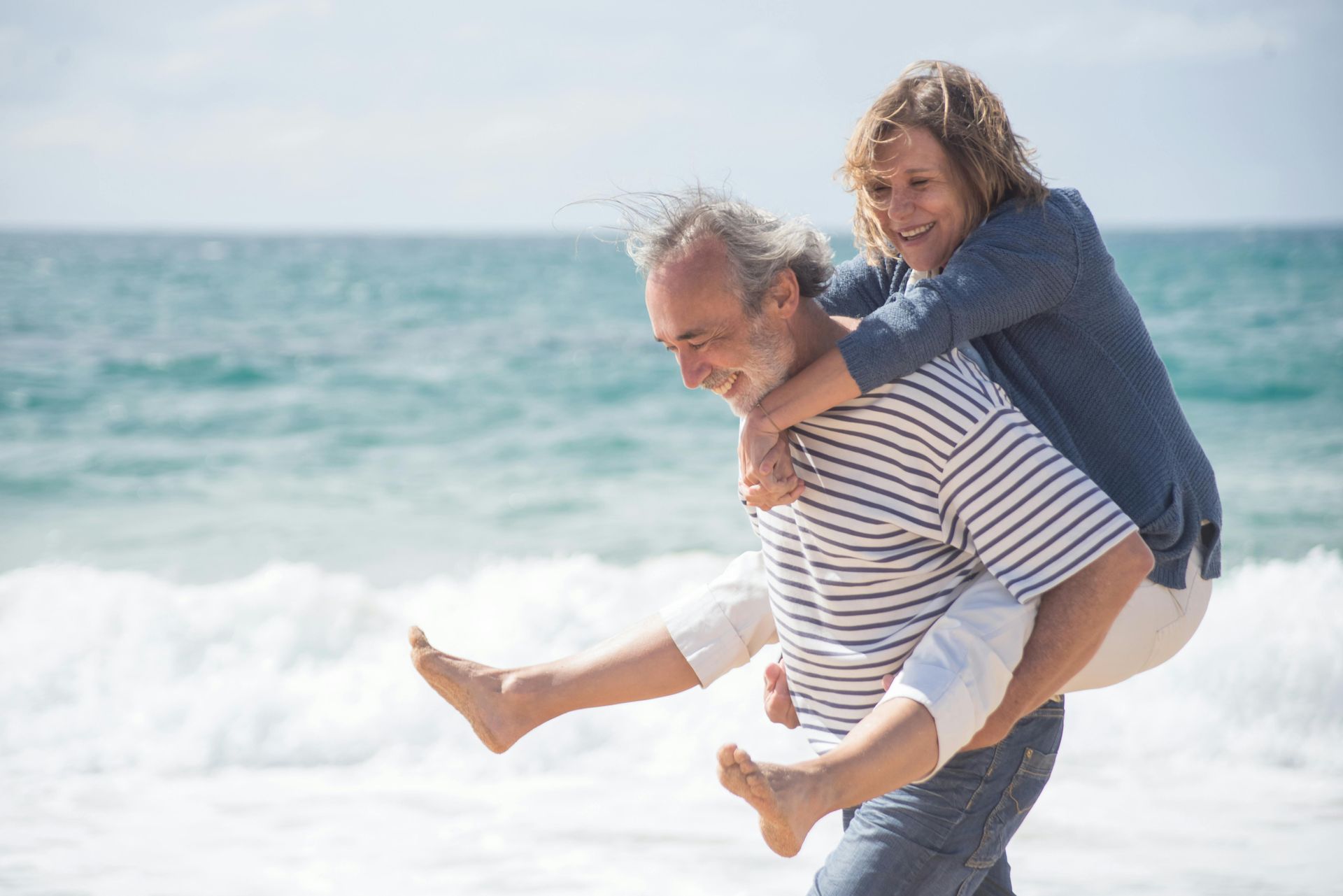 Man carrying a smiling child on his back at the beach with ocean waves behind them