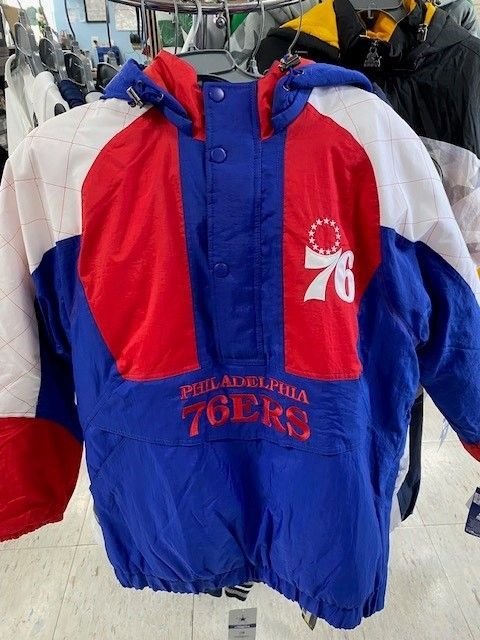 Philadelphia 76ers blue, red, and white hooded jacket hanging on a clothing rack