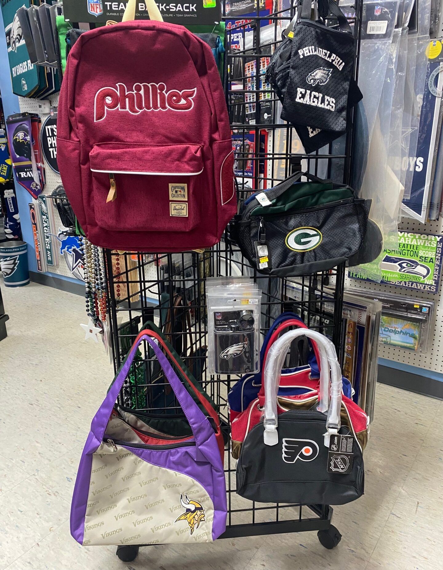 Backpacks and tote bags displayed on a retail rack, including Phillies and Packers bags
