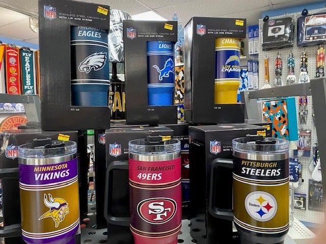 NFL team-colored tumbler cups displayed in a store shelf, including Eagles, Vikings, 49ers, Steelers, and Lions logos