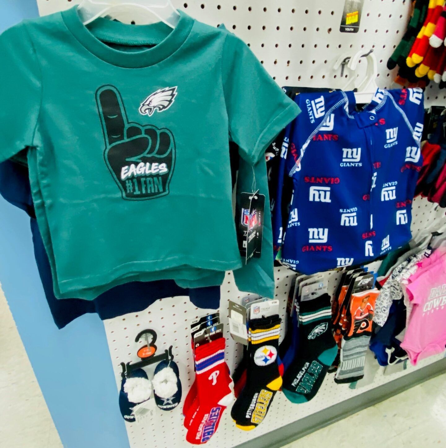 Children’s sports shirts and socks displayed on a store shelf, including teal and blue Philadelphia Eagles gear