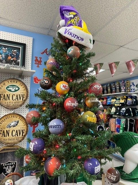 Christmas tree decorated with NFL team ornaments in a sports-themed room, topped with a Vikings logo