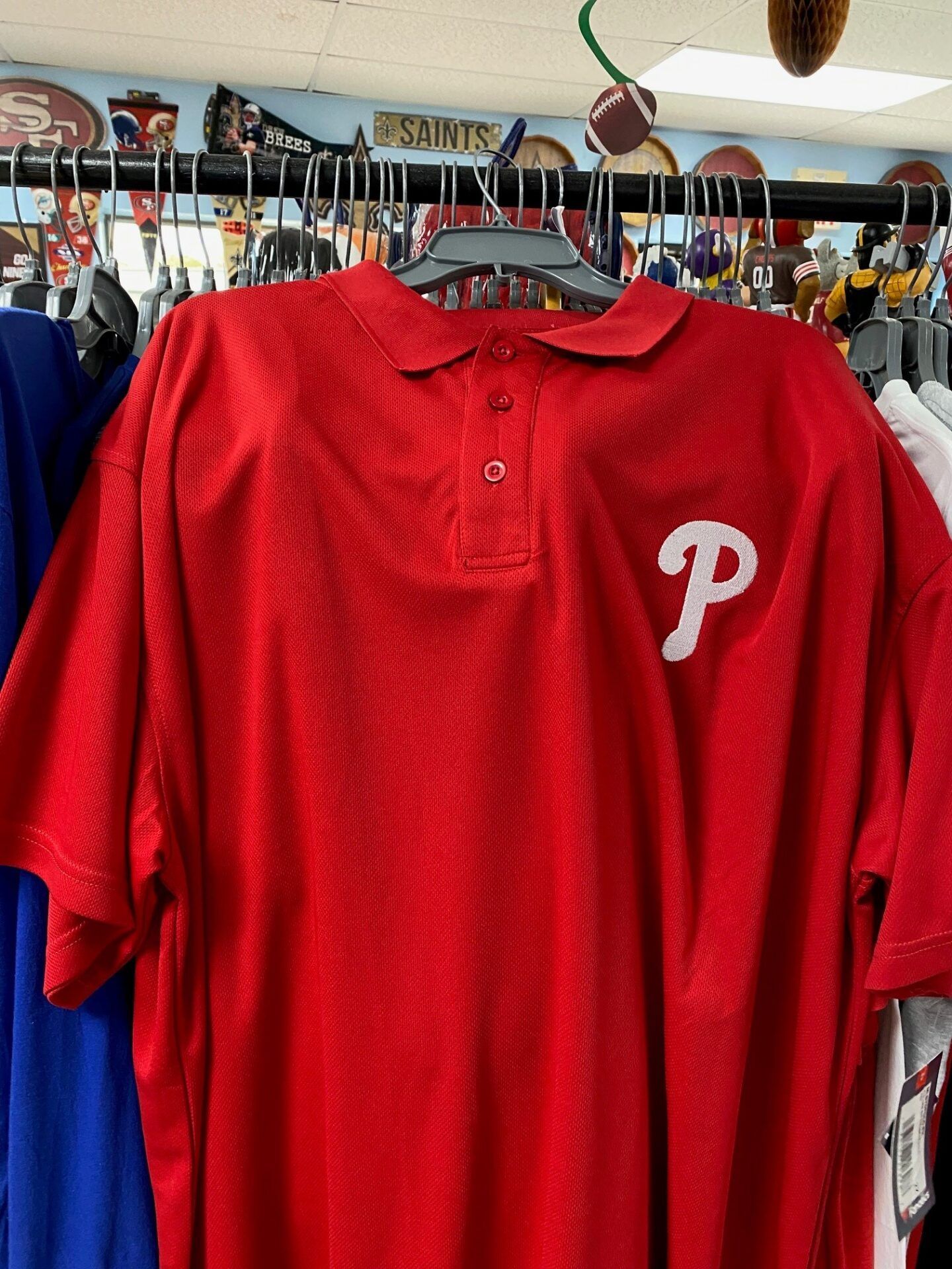 Red Philadelphia Phillies polo shirt hanging on a rack at a clothing store.