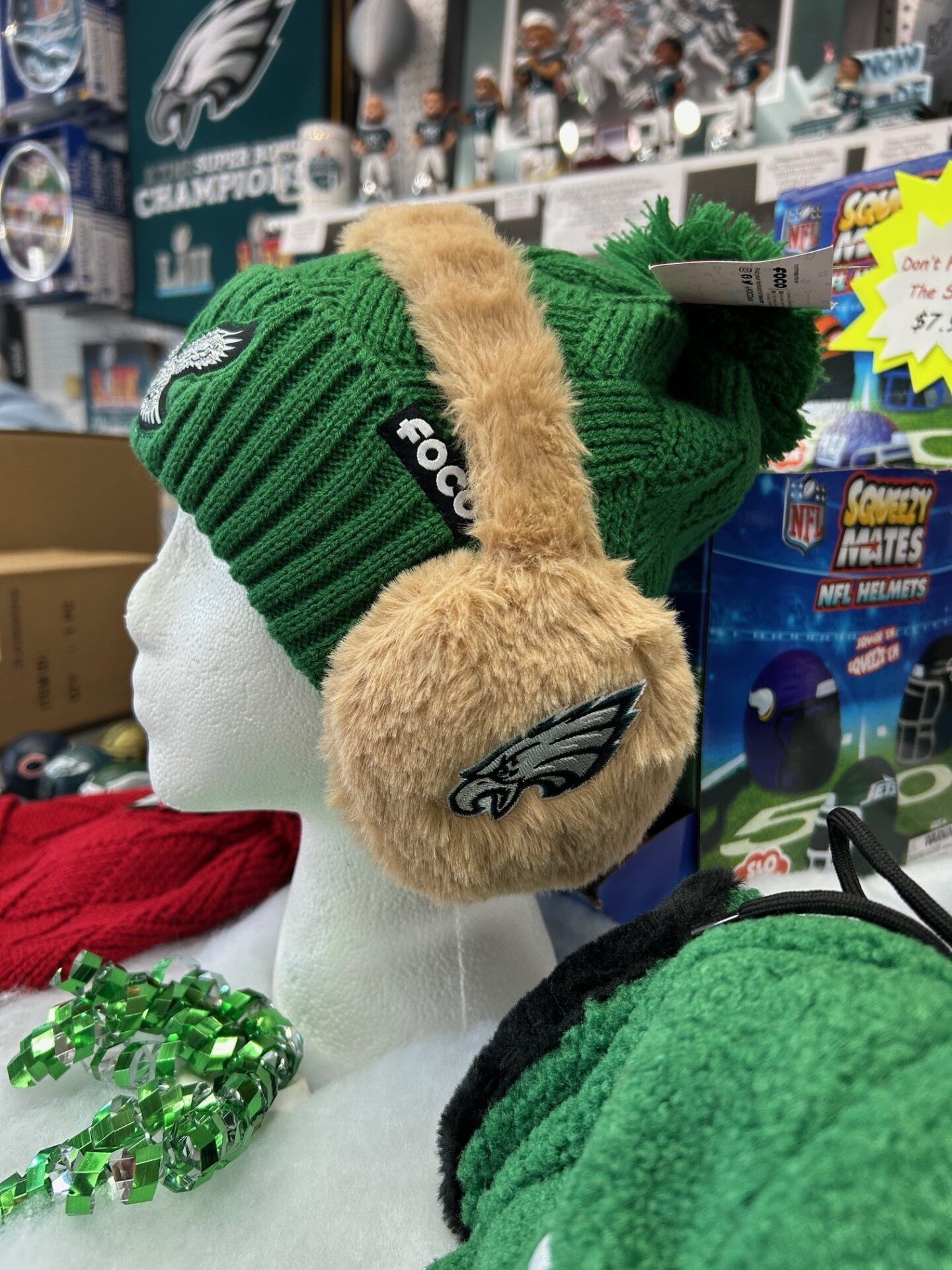 Green Eagles knit hat with tan fuzzy ear flaps on a white mannequin in a sports shop