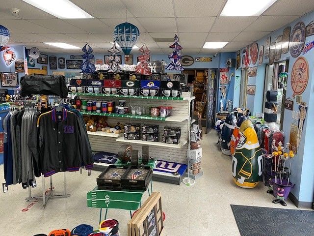 Collectibles shop interior with sports merchandise, racks of clothing, shelves, and team memorabilia