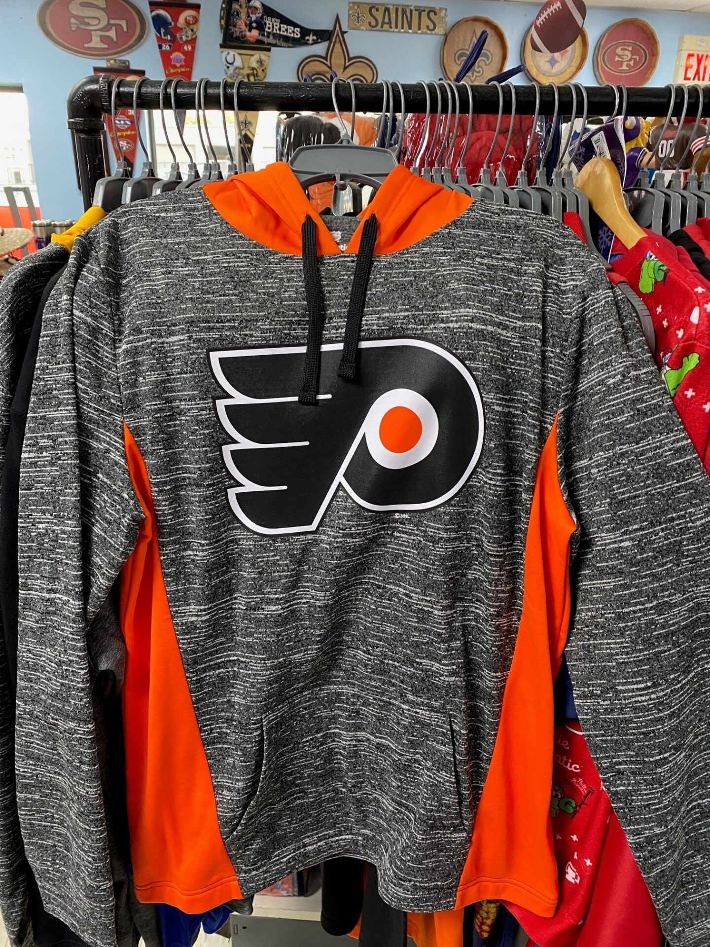 Philadelphia Flyers hoodie hanging on a rack, gray with orange accents and team logo.
