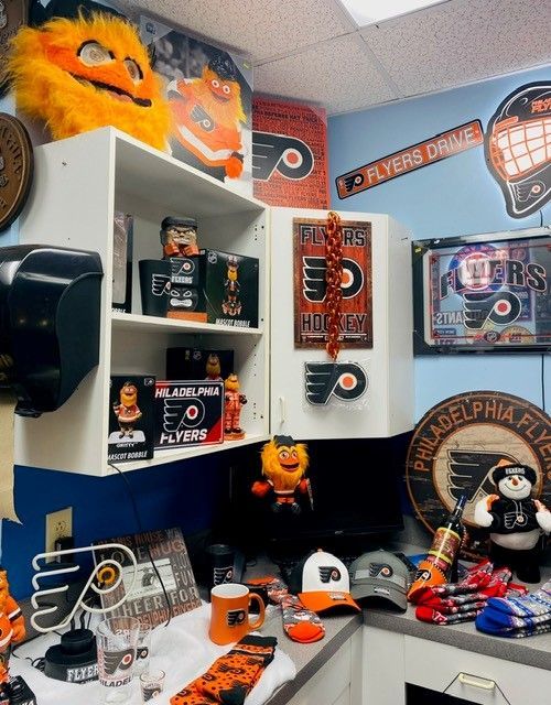 Flyers-themed office nook with orange-and-black decor, memorabilia, and sports artwork on shelves and walls