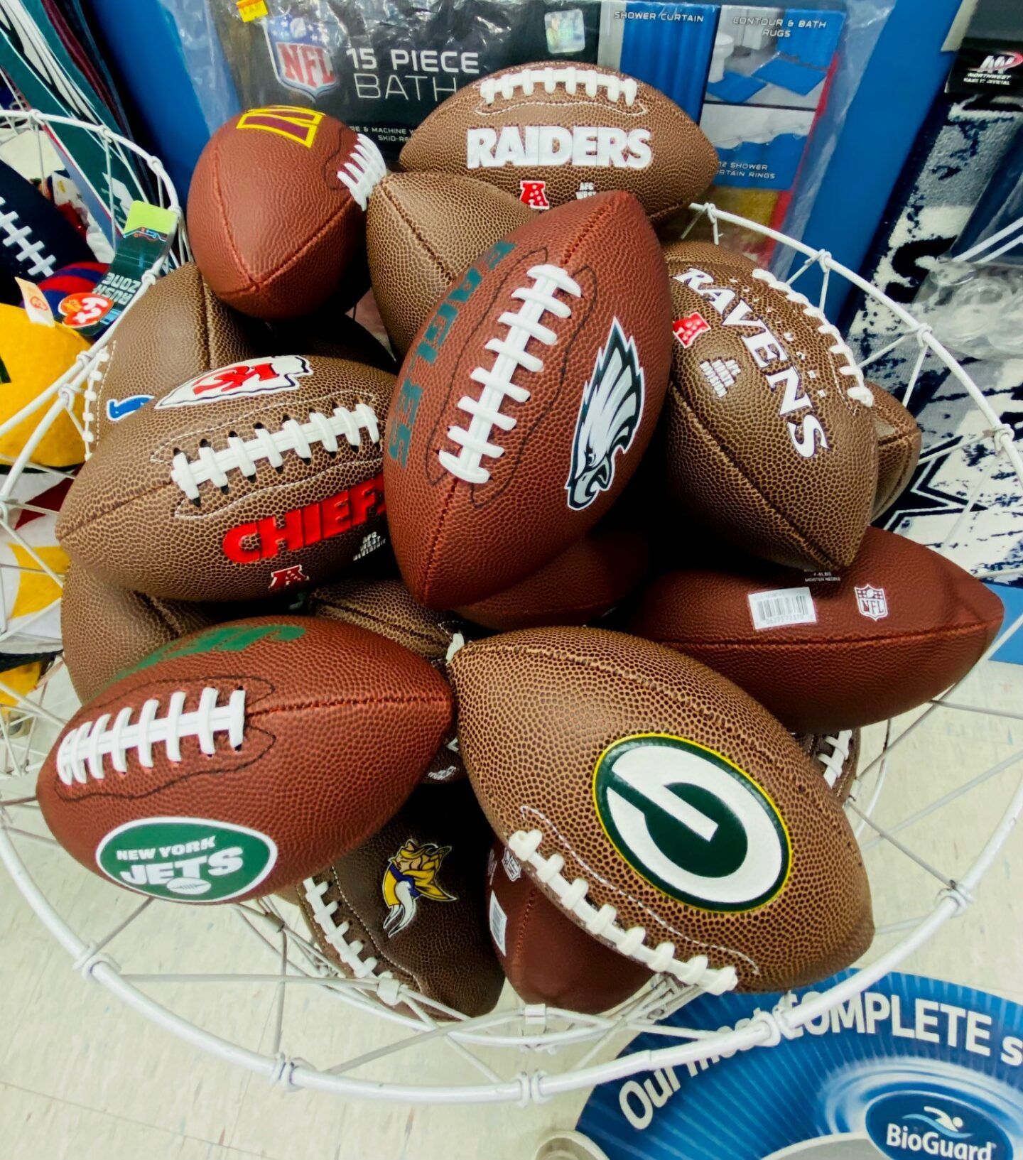 Assorted NFL footballs in a wire basket, including Raiders, Chiefs, and Jets logos