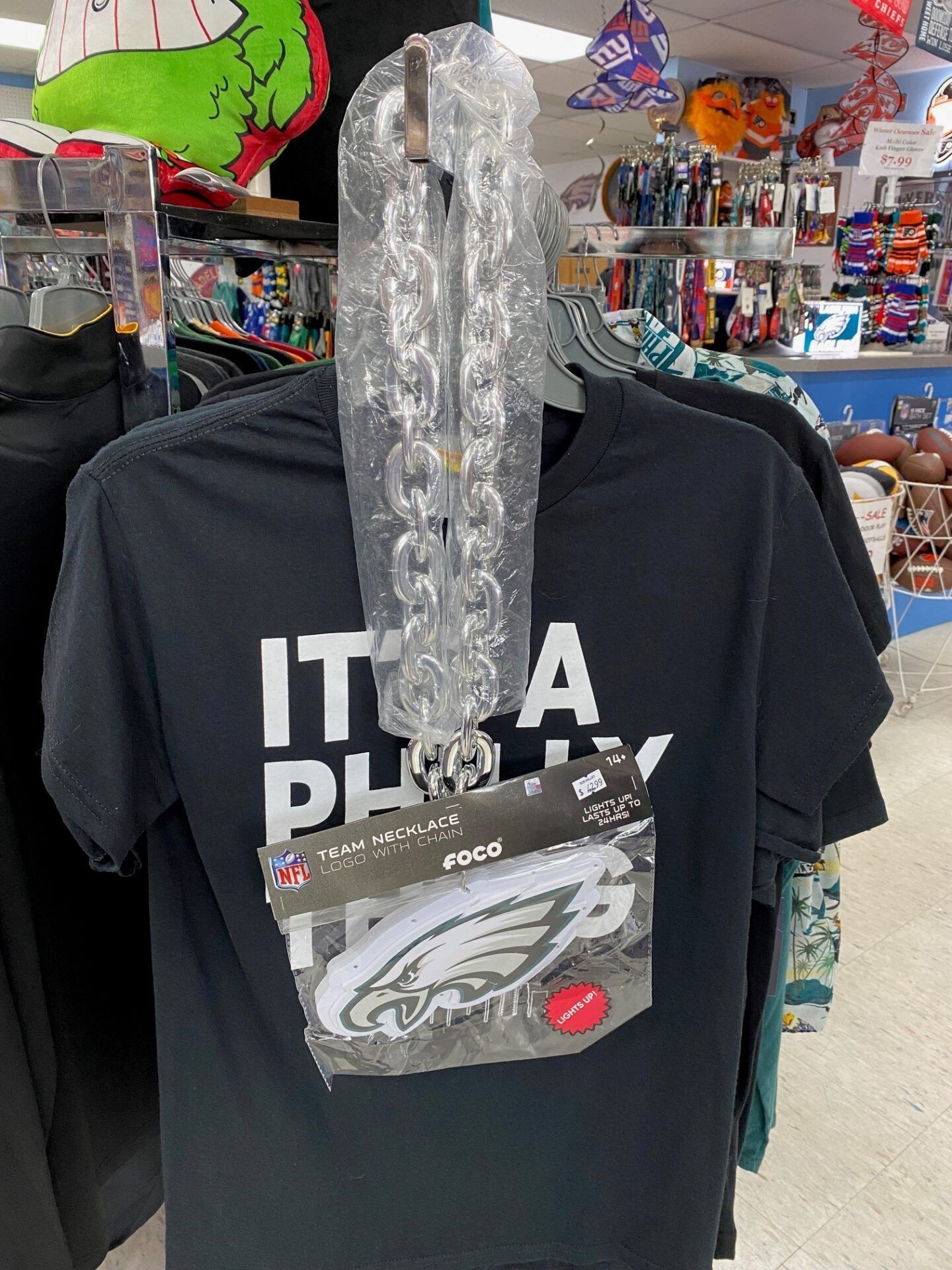Black T-shirt on a store mannequin with a hanging package in a colorful retail shop.