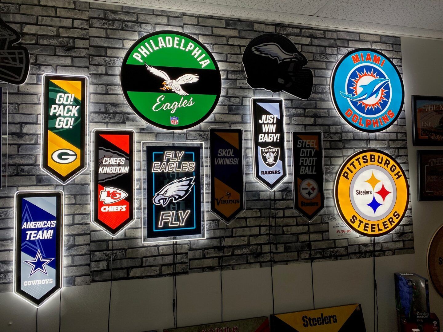 Wall of sports team pennants and signs displayed on a gray brick wall indoors