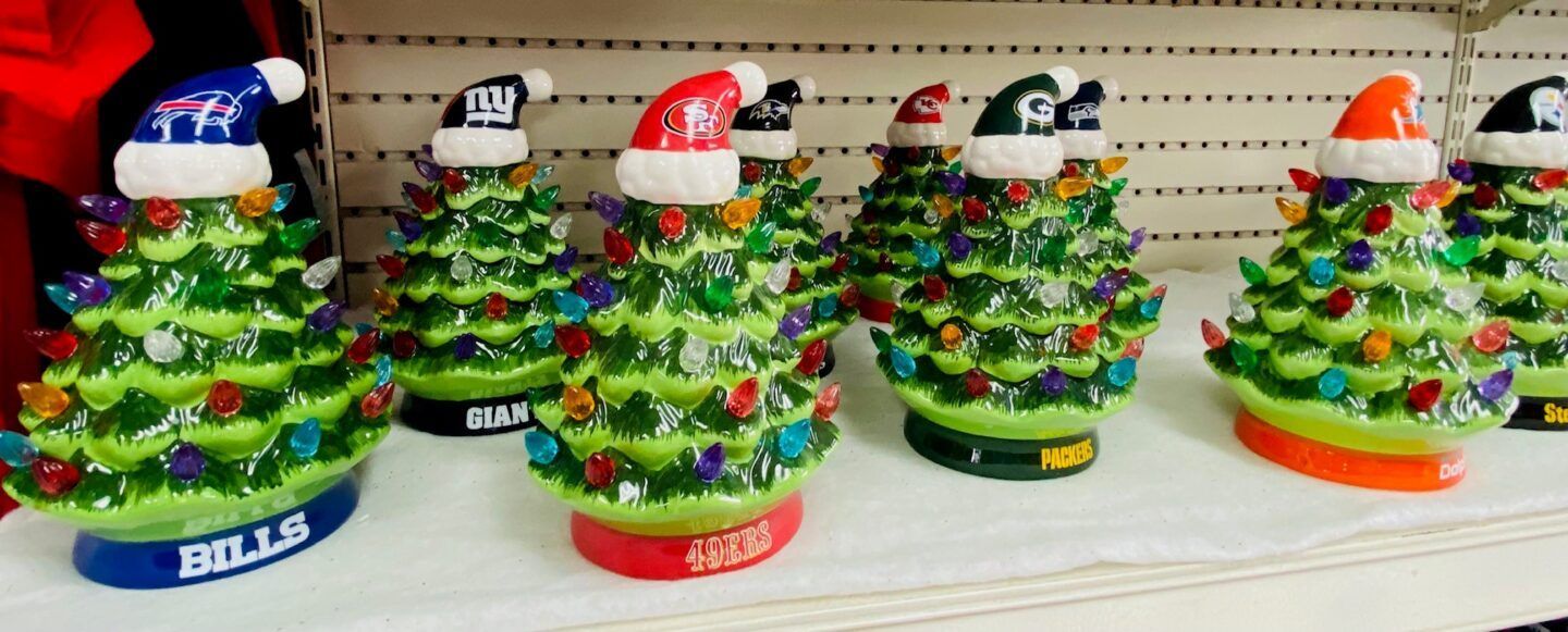 Colorful Christmas tree figurines with sports team hats and bases lined up on a table