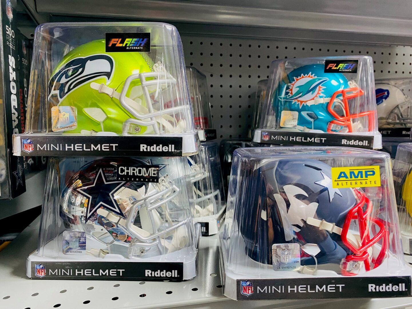 Store display of NFL mini football helmets in clear cases on a pegboard shelf, mostly white, black, and blue helmets