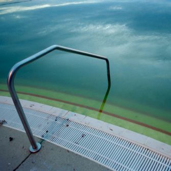 Pool ladder beside turquoise water with a metal deck railing and tiled edge