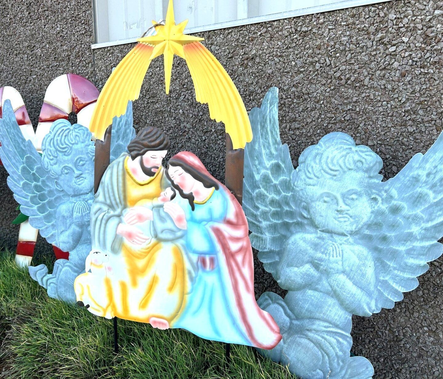 Colorful nativity display with Mary, baby Jesus, angel wings, and a star under a yellow arch outdoors