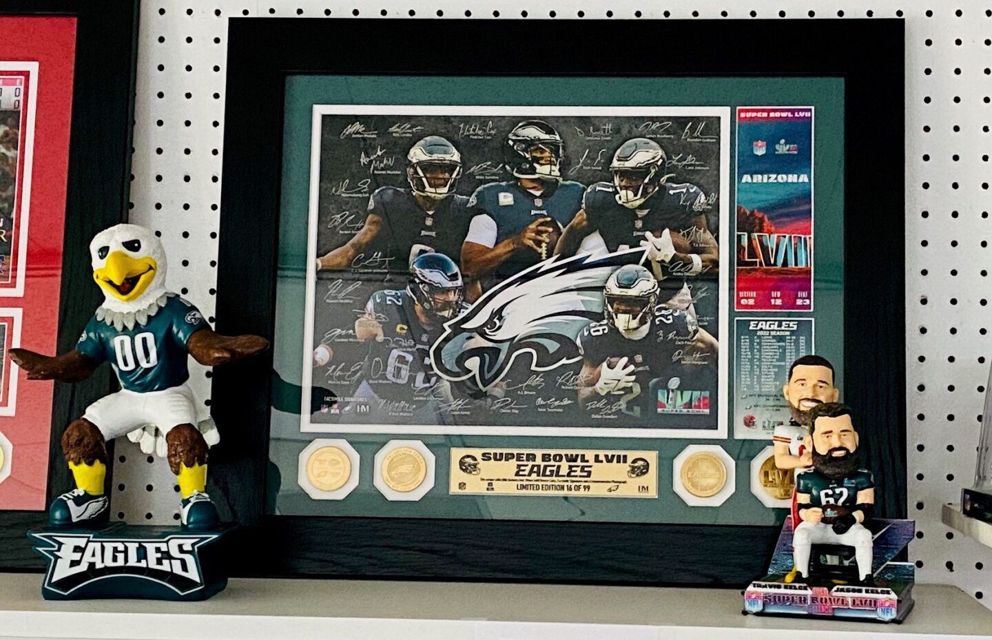 Framed Philadelphia Eagles collage with two Eagles figurines on a shelf against a pegboard wall
