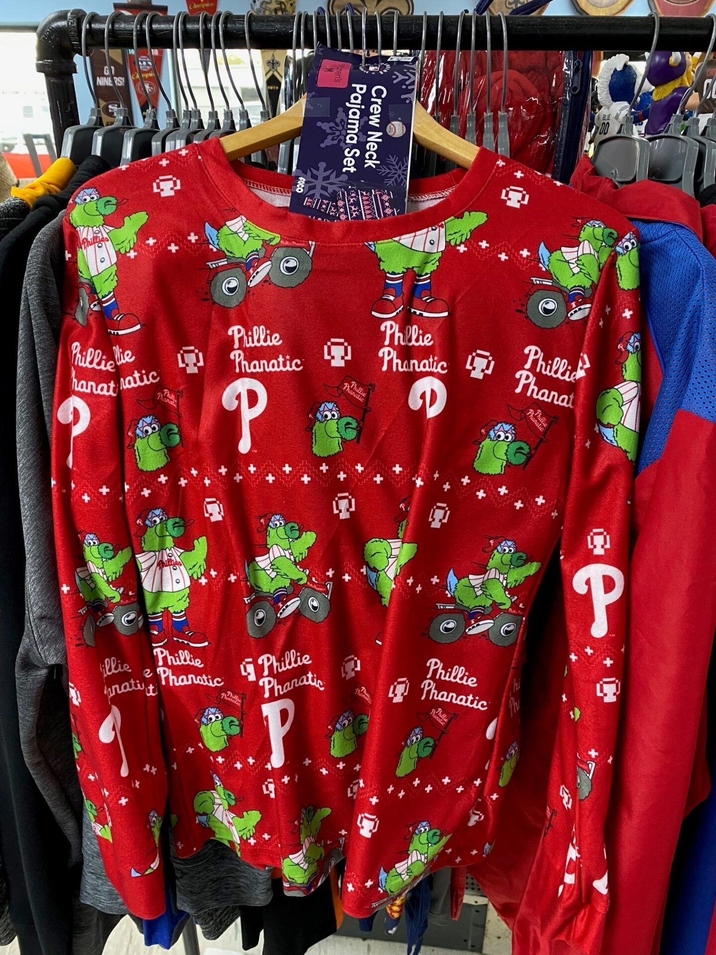 Red holiday sweater with green Grinch faces and white Christmas designs on a clothing rack